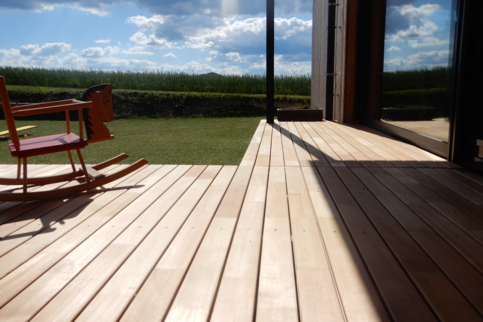 Eine Holzterrasse, auf der ein Schaukelpferd steht, im Gegenlicht der Sonne.